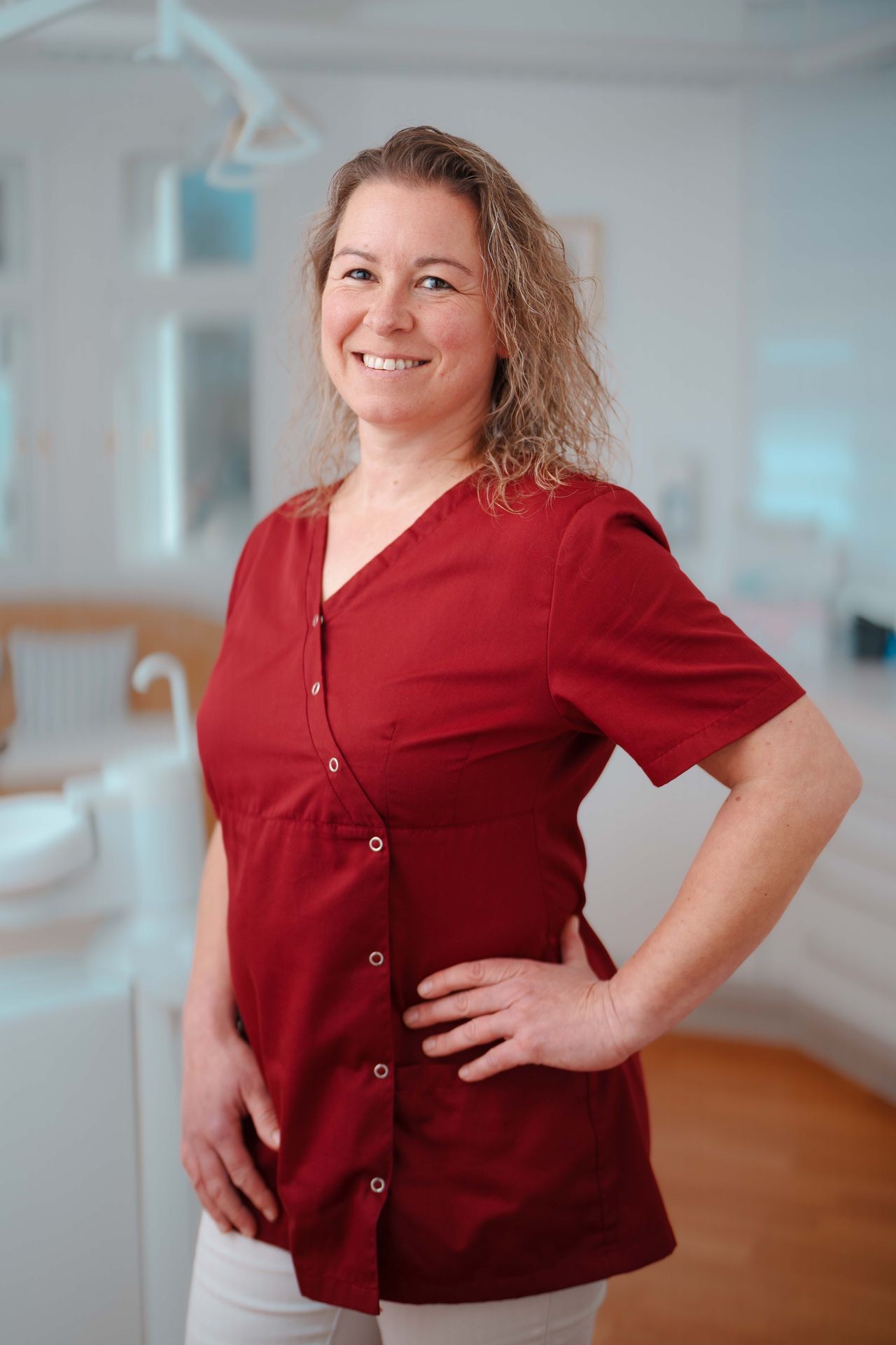 Frau in rotem Outfit steht in einer hellen Praxis am Inn mit moderner Zahnarztausstattung.