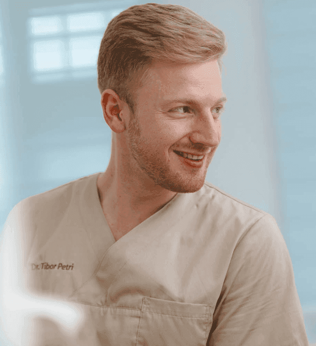 Dr. med. dent Tibor Jonathan Petri bei in beigem Praxiskittel wie er einem Patienten zulächelt