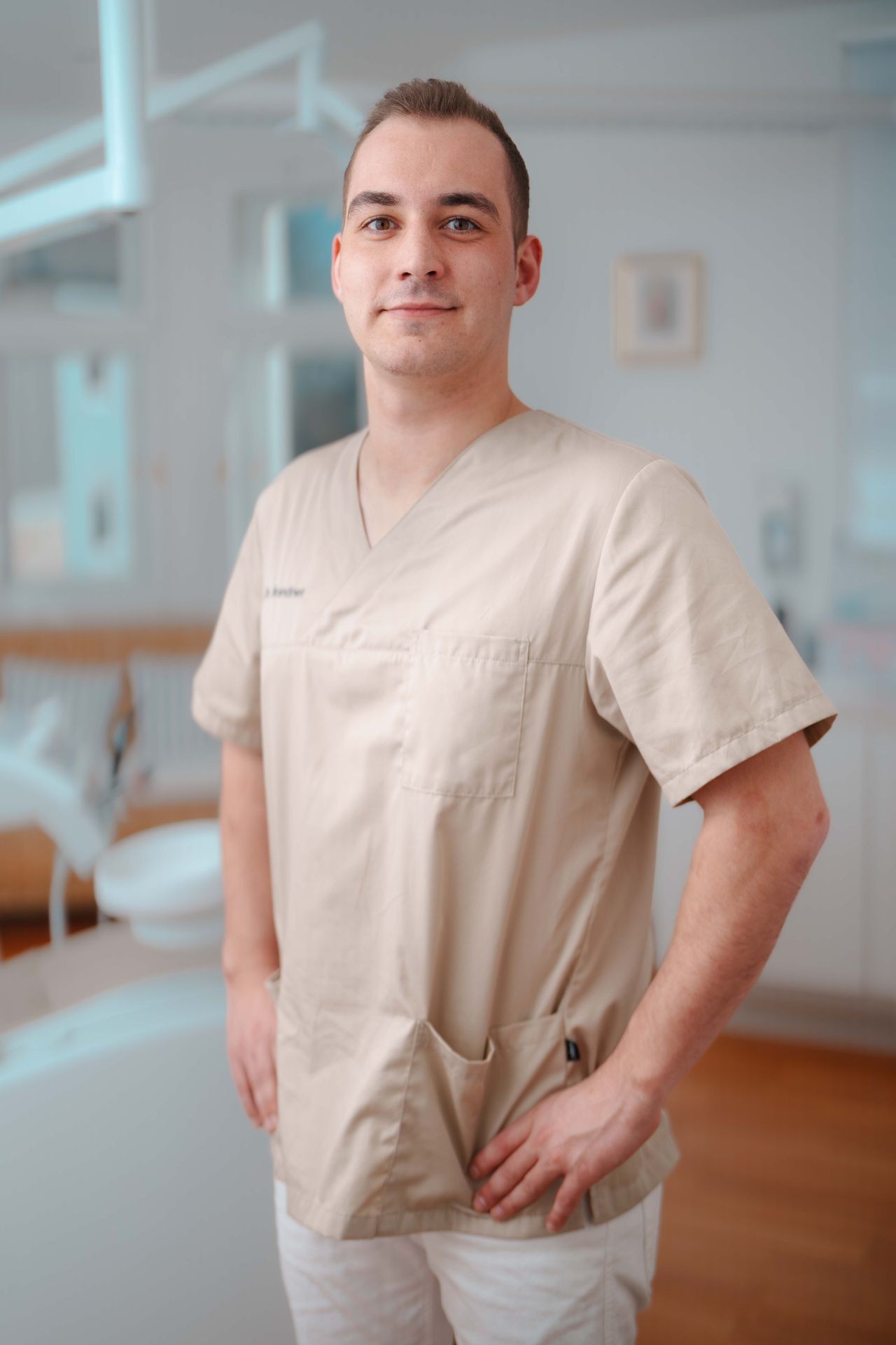 Dr. Tibor Petri Lächelnd in beigen Kitteln steht in hellem medizinischem Büro mit Händen an der Hüfte