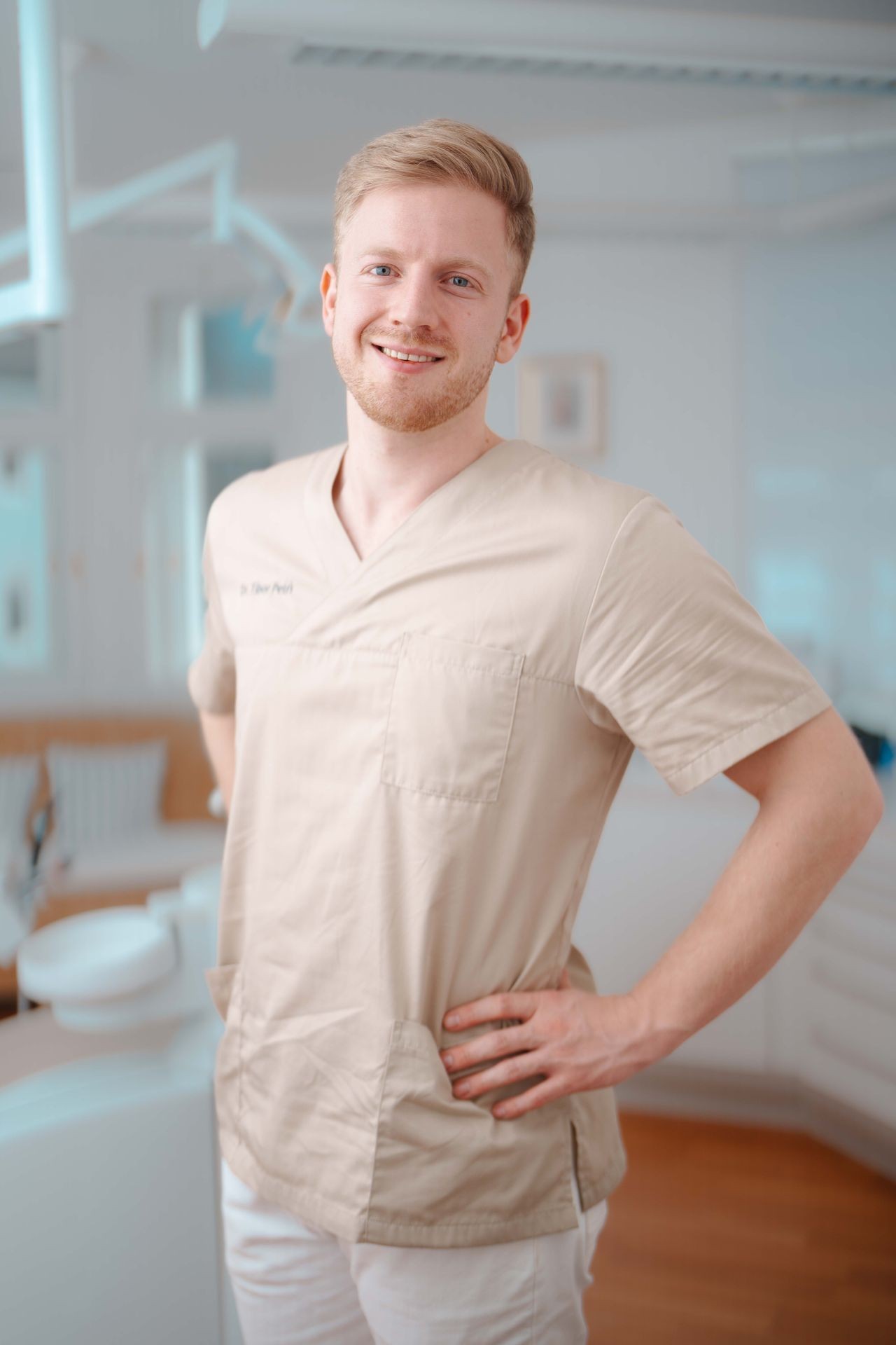 Dr. Tibor Petri Lächelnd in beigen Kitteln steht in hellem medizinischem Büro mit Händen an der Hüfte