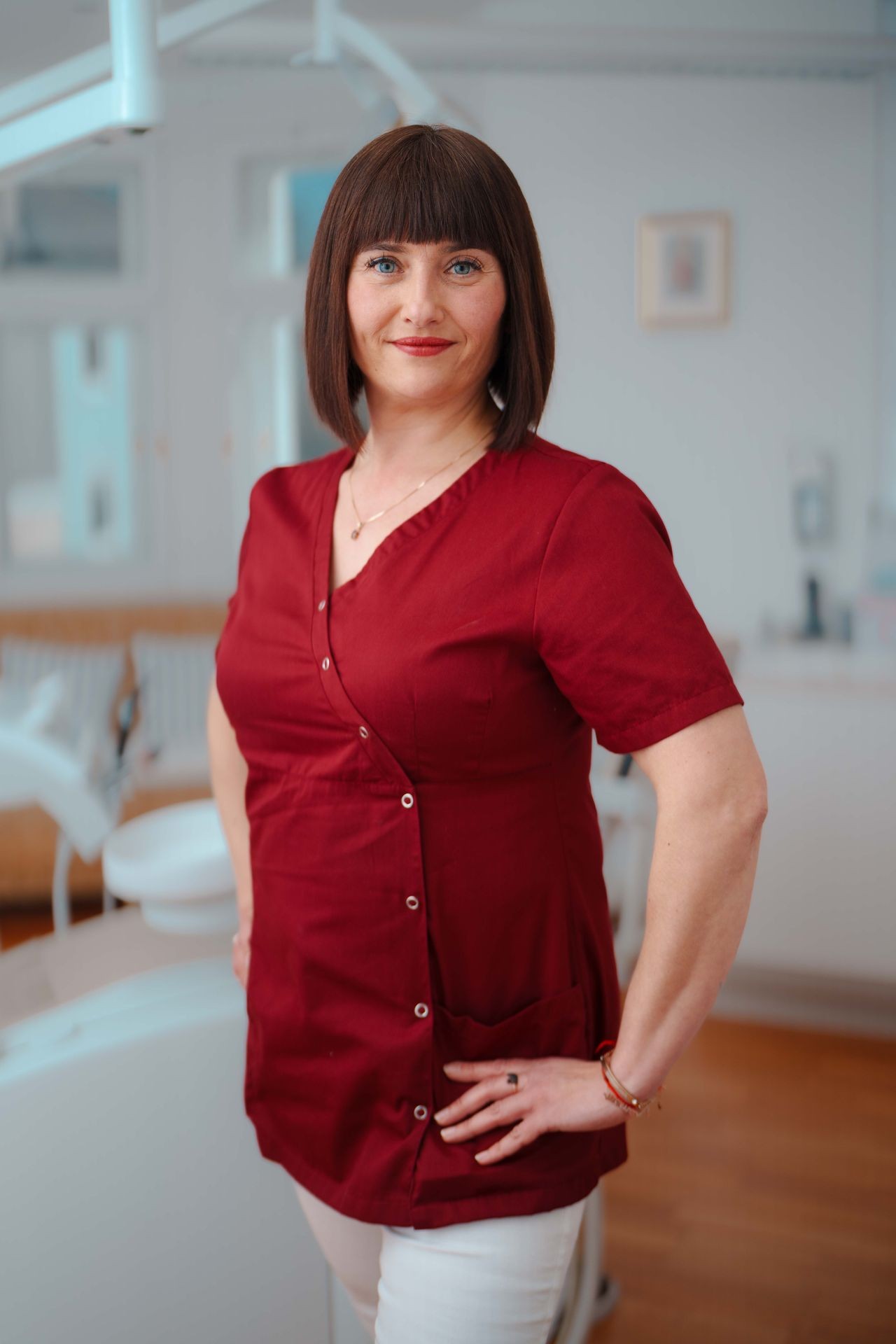 Frau in rotem Outfit steht in einem hellen Raum mit moderner Zahnarztausstattung.