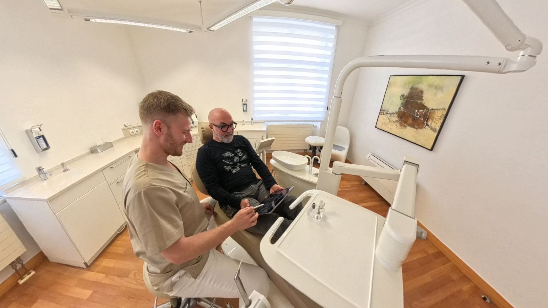Dr. Tibor Petri und Patient besprechen digitale Zahnbilder auf Tablet im modernen Behandlungsraum